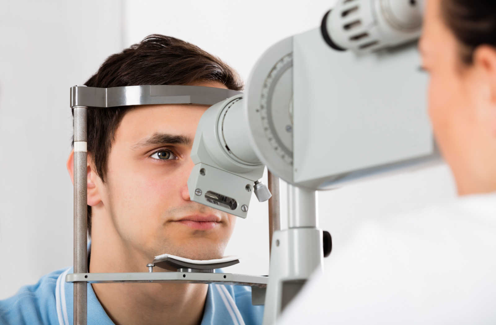 A man sitting in an optometrist's office looking into a machine that tests his eyes for dry eye syndrome. 