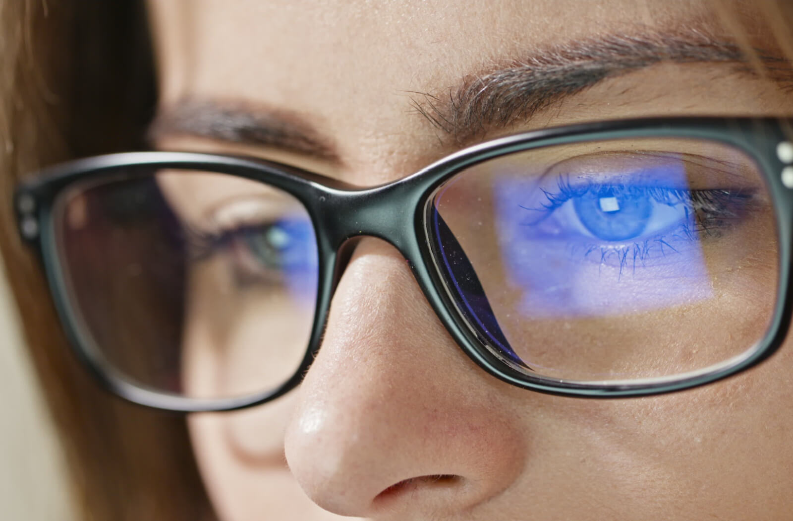 A close-up shot captures a young woman wearing computer glasses, with the computer screen reflecting in her eyewear.